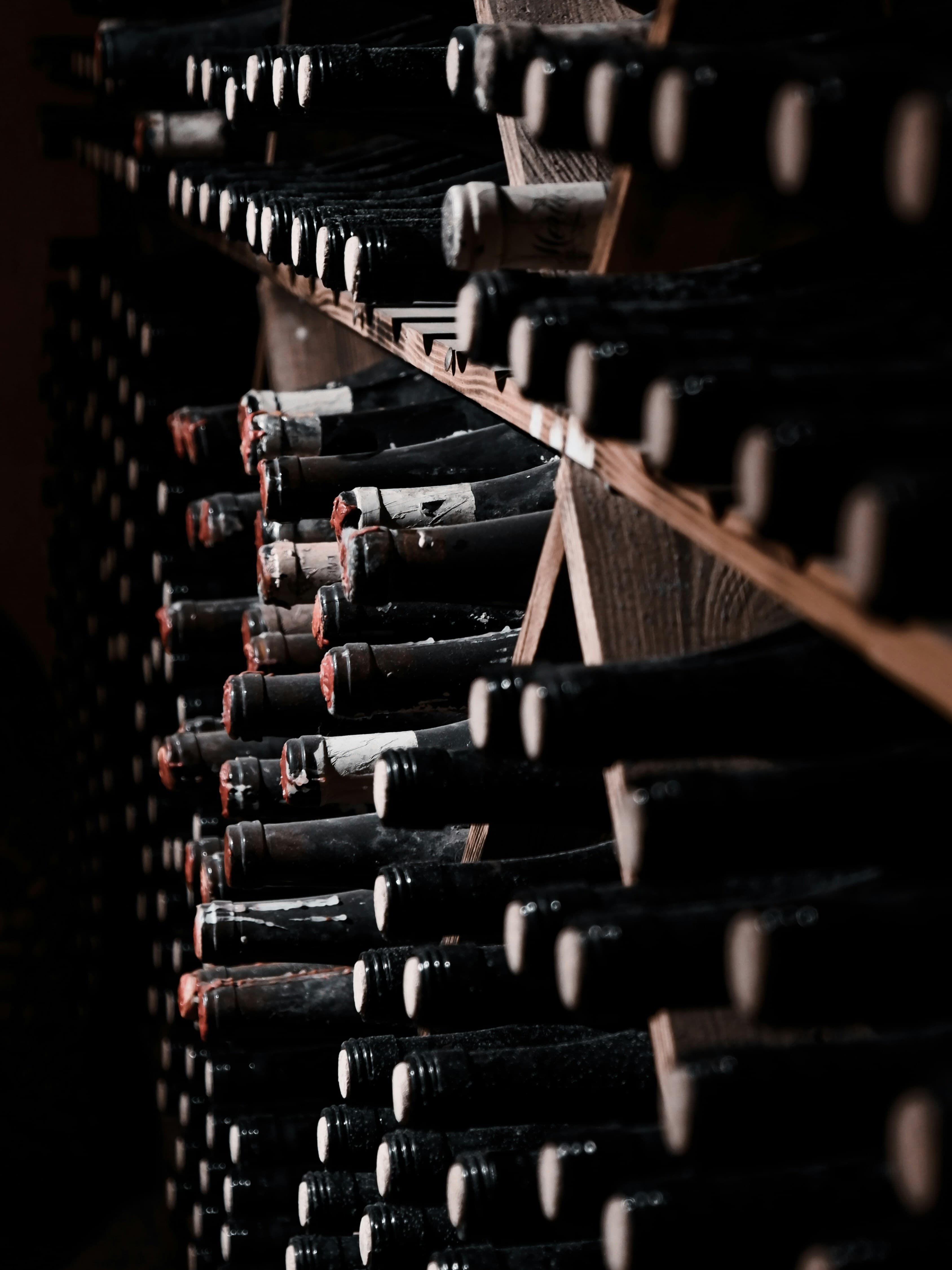 Vintage wax-dipped wine bottles aging in dark wooden racks